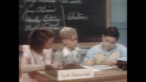 1940s: Boys and girl write on papers and talk at desk in classroom. Hand with pencil corrects punctuation and capitalization on typewritten paragraph.
