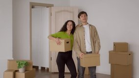 New House. Happy Couple Holding Cardboard Moving Boxes Standing At Home After Relocation. Real Estate Rental. Family Housing, Purchase And Ownership Concept. Slow Motion