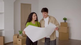 Real Estate. Happy Couple Holding Paper With Renovation Plan Standing Among Cardboard Moving Boxes At Home. Relocation, Hew House Ownership Concept. Slow Motion