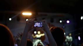 Spectator at a concert is filming a performance on a mobile phone. Multi-colored lights at a concert.