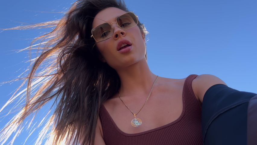Latina brunette shoots herself on camera in summer on the beach in sunglasses. The wind blows the girl s hair. Model spins on phone at sunset on Santa Monica Pier