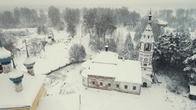 Fairy snowy rural landscape and church, winter, aerial view. White snow is falling, cloudy weather, copy space. Screensaver, footage for intro, background, titles. UHD 4K.