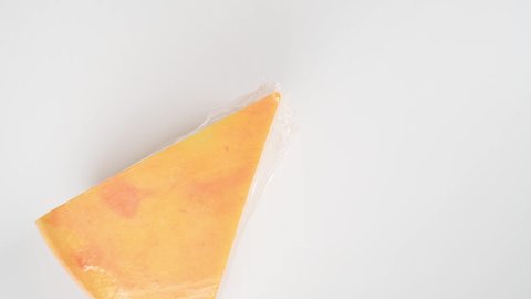 Hands of young woman picks up large piece of hard cheese in package on white background top view. Fresh tasty cheese, dairy food, cooking ingredient. Sealed piece of cheese in factory transparent film