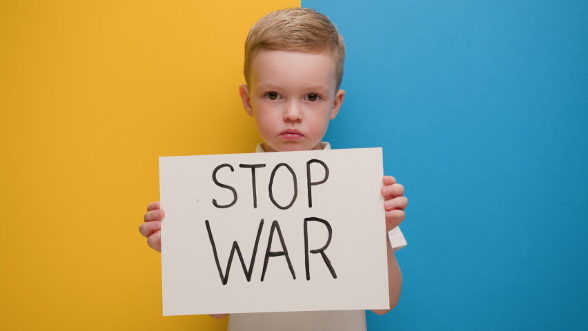 Portrait serious blond 4-year-old boy protesting war raises banner with inscription Stop War at blue yellow flag of country Ukraine. Call to stop war, child against war, crisis in Ukraine. | Shutterstock HD Video #1087380470