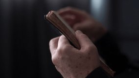Close-up hands of unrecognizable mature adult man reading older book and flipping pages in dark room. Closeup cropped shot of senior aged man reading novel and flip through pages of book. - Powered by Shutterstock - Get 15% off with code: PIKWIZARD15