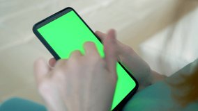 Woman using mobile phone sitting on a sofa at home. 4k video footage with green screen smartphone