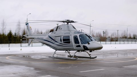 beautiful silver color private business helicopter with blue stripes stands parked on helipad. In winter, businessman flew to important business meeting on air vehicle.