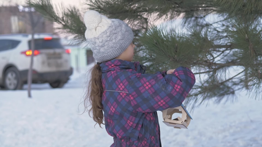 Child, little girl feeding birds in winter. Bird feeder in snowy tree, helping birds during cold season, teaching kids to love and protect nature