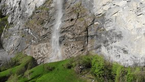 Aerial video of impressive Lauterbrunnen waterfall in Switzerland. Water falling down a tall rocky cliff with snowy mountain range and green trees in the background. Swiss alps and picturesque valley.