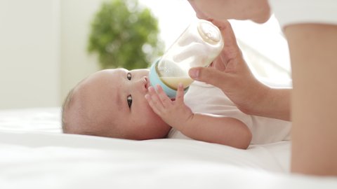 Mother feeding milk to Asian newborn baby on white bed