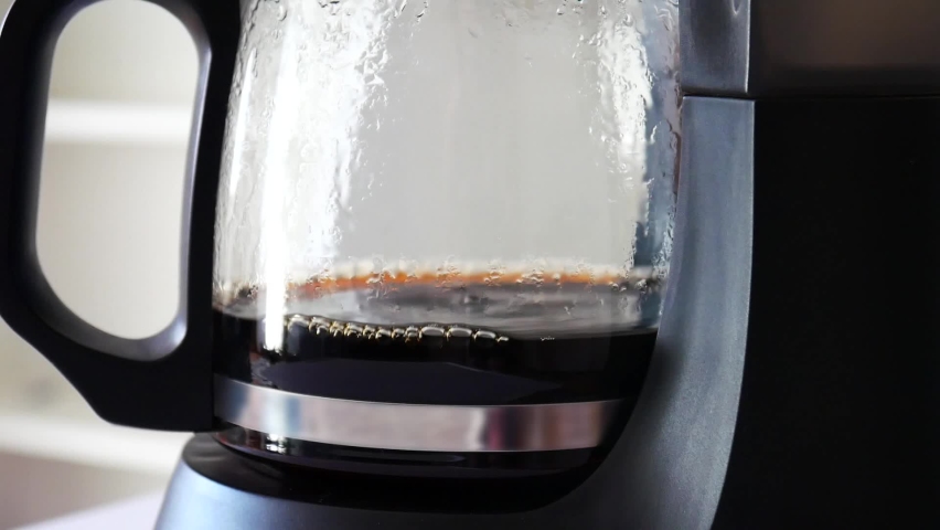 Droplets of brewed coffee drip slowly into the coffee pot mounted on the platform of a black coffee maker | Shutterstock HD Video #1087396289