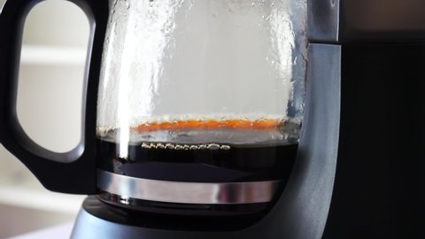 Droplets of brewed coffee drip slowly into the coffee pot mounted on the platform of a black coffee maker