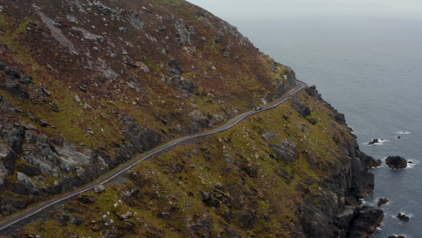Breath taking shot of slowly moving car on narrow panoramic route in steep slope above sea coast. Dangerous road around Slea Head. Ireland