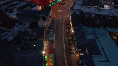 Fly above illuminated street in city. Colourful house facades along road in town centre at night. Killarney, Ireland