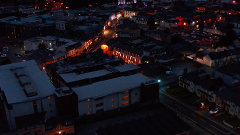 Vivid colour illuminated houses along streets in town centre. Backwards fly above evening city. Killarney, Ireland
