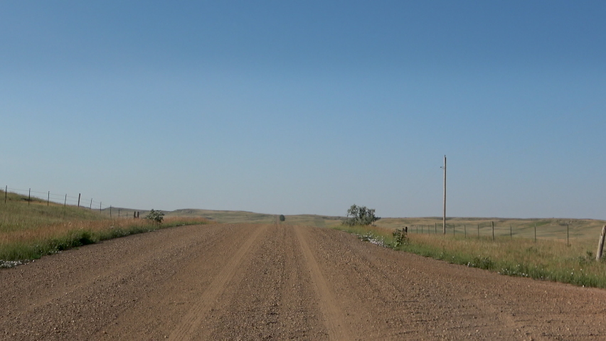 Driving along a straight dirt road in Montana on a summer day