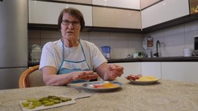 65 adult woman tells culinary recipe for her blog, sitting in kitchen and looking at camera. Elderly mother's hobby.