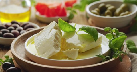 Feta cheese with olive oil with addition fresh basil leaves, close up view. Traditional greek product.