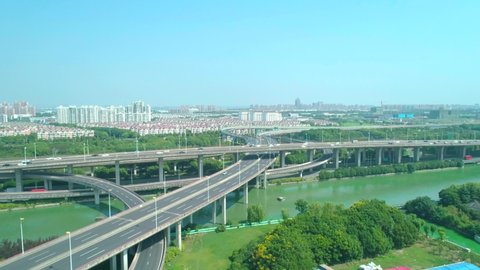 Aerial view of a highway overpass multilevel junction with fast moving cars surrounded by green trees and with a river on a side on a sunny day