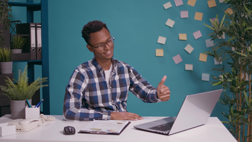 Positive employee giving thumbs up in front of laptop screen, showing approval and good symbol with hand. Confident person doing okay sign and confirming success satisfaction.