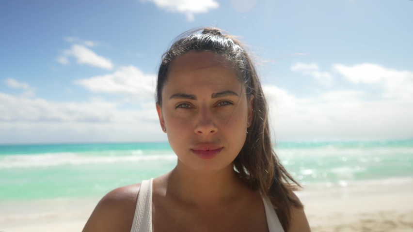 Happy young woman standing at Cancun Beach. Sensuous female with windswept hair is looking at the camera. She is wearing white bikini top during summer vacation at Cancun Mexico.