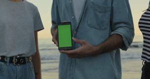Three friends standing on beach and text messaging in front of sea