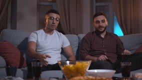 Young men watch tv match and get upset while sitting on couch in dark living room spbas. 4k video Front view of two sports fans browse football and support team, show sad emotions and sit on sofa in