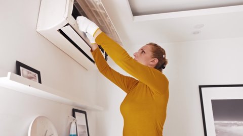 Woman cleaning aircon filters indoor unit at home.