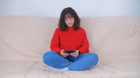 Happy white woman browsing tablet computer on couch at home. Cheerful young female using modern gadget for web surfing in living room. Pretty millenial person reading news on tablet pc