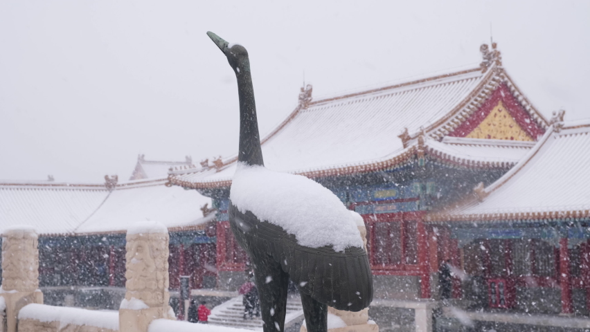 Bronze crane stands in heavy snow, Forbidden City, Beijing, China, with background of imperial halls.
