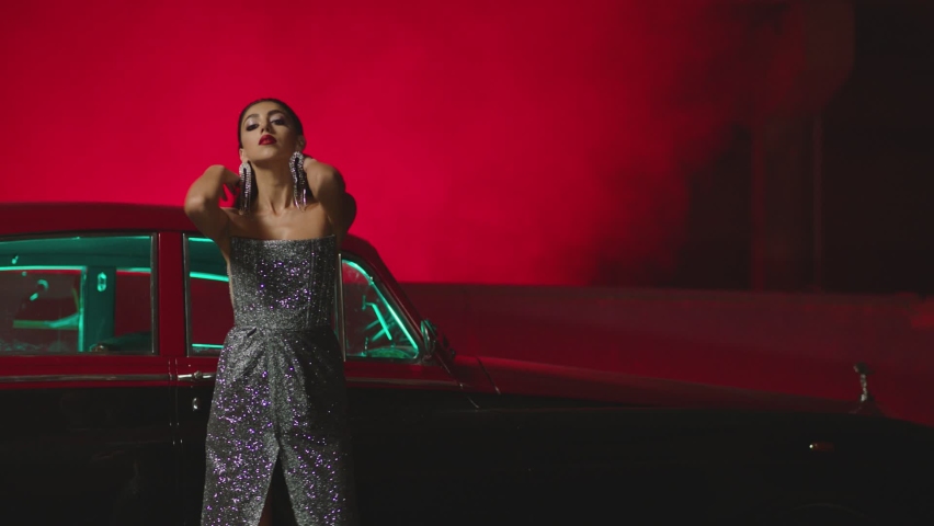 Beautiful Elegant Young Woman Standing , Dancing and Flirting near old retro classic car. Old fashioned luxury style concept . Rich fashion lifestyle . Luxury dress with fabric glitter, spangles .
