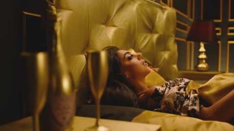 Beautiful Young Woman Sleeping Dreaming and Flirting in Bed . Female model resting lying asleep inside luxury golden bedroom . Golden room in hotel , house . Shot on ARRI cinema camera in slow motion