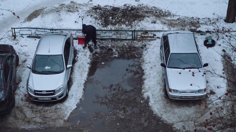 A man removes snow in winter under a place for a car in the rain