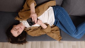 Selective focus of happy young woman watching video looking at smartphone relaxing on couch, cute smiling girl enjoying using online mobile apps for education or entertainment on cell phone at home