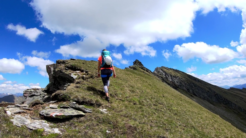 Woman walking on a hiking trail admiring the panoramic view from Reitereck in Carinthia, Maltatal in the Austrian Alps. Endless mountain chains in the High Tauern. Outdoor activity. Wanderlust
