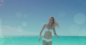 Animation of light spots over caucasian woman walking on beach. walk day and celebration concept digitally generated video.