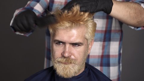 Hairdresser combing man hair. Process of a guy having hair dyed at hairdresser salon. Dyed blond hair for a bearded hipster guy.