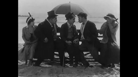 CIRCA 1915 - In this silent comedy, a man (Charlie Chaplin) tries to flirt with a woman at a beach until men trying to fight him catch up.