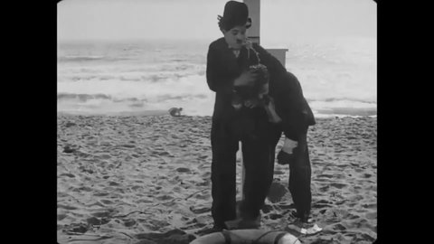 CIRCA 1915 - In this silent comedy, a man (Charlie Chaplin) tries to subdue a bum and flirt with a woman on the beach at the same time.