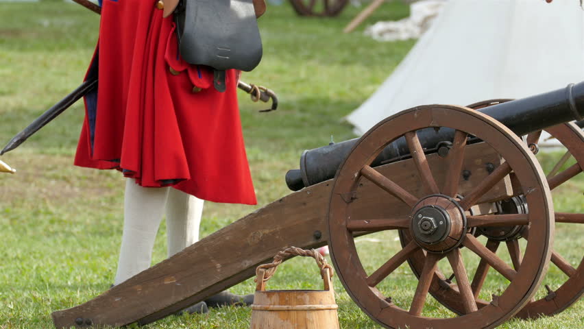 Guards are ready to fire up the small cannon on the ground. The guards are holding a stick with the fire on it