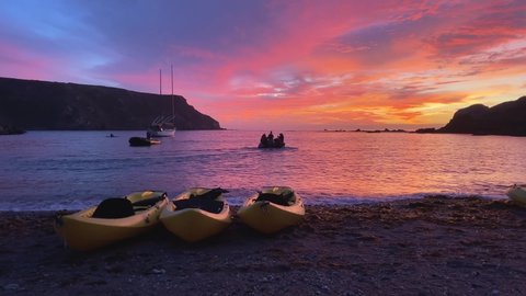 CATALINA, CALIFORNIA - CIRCA 2022 - Kayaks rest on the beach of Catalina at sunset while people sail on other vessels.