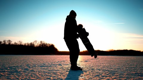 Priceless parenthood moments. Silhouette happy dad and little son run in winter park at sunset. Beautiful sunset in the winter park.