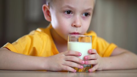Boy holding a glass in her hands and drinks milk. Little boy drinks milk. Happy child has breakfast at home. Healthy child having breakfast.
