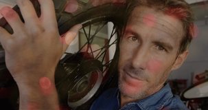 Animation of flickering lights over caucasian male mechanic holding motorcycle wheel. motorcycle safety awareness month concept digitally generated video.