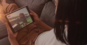 Animation of glowing lights over biracial woman watching football on tablet. sports, competition and technology concept digitally generated video.
