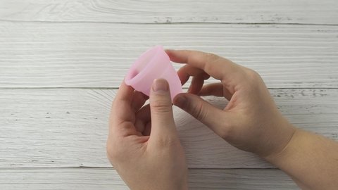 Woman hand holding menstrual cup and demonstrating labia folding methods. Intimate menstruation hygiene period. Zero waste alternative medical silicone products. Female health concept