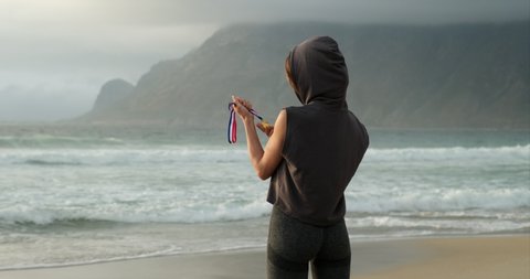 woman hand raised, holding gold medal against sky. female athlete stands on the beach and proudly holds a gold medal in her hand after winning the competition. Gold medal for first place