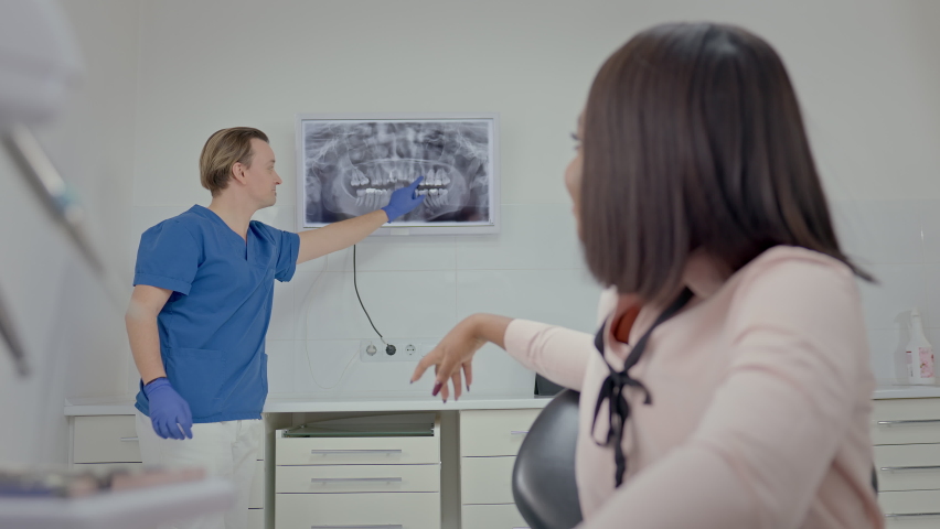 Male Dentist In Dental Office Shows Patient Image Of Her Teeth On Big Screen.