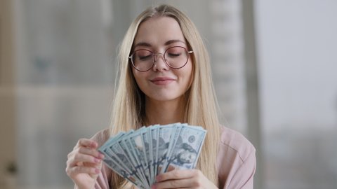 Happy caucasian business woman in glasses rich successful girl winner female throws money in air rejoices with banknotes gets financial benefit victory scatter dollars win indoors close up portrait