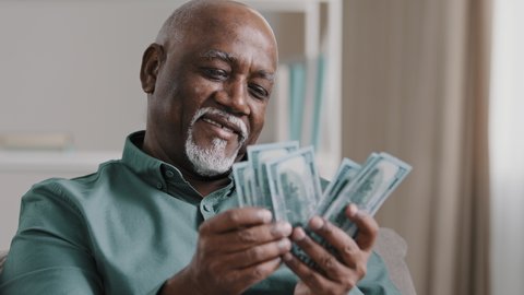Happy african american satisfied winning bet elderly retired man counting savings mature male with pile dollars counting banknotes successful business investment profit in currency comfortable old age